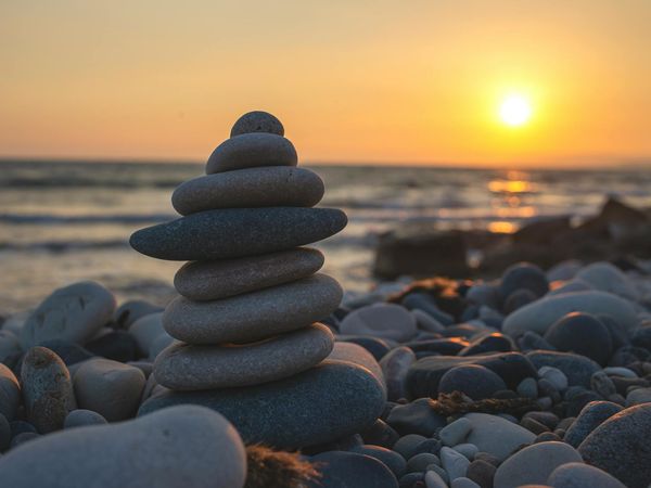 Symbolic image of a balanced stone cairn on a peaceful beach at sunset.
